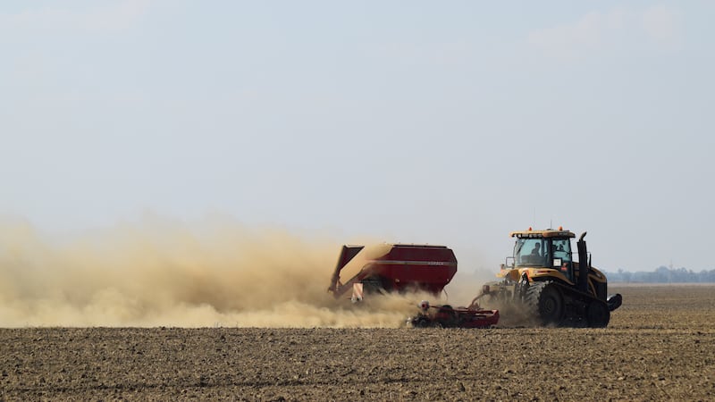 Tractor rides on the field and puts fertilizer into the soil.