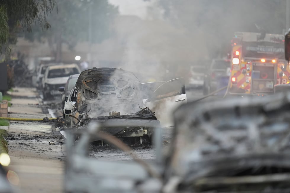 Vehicles are damaged as authorities work the scene where a small plane crashed into a San...